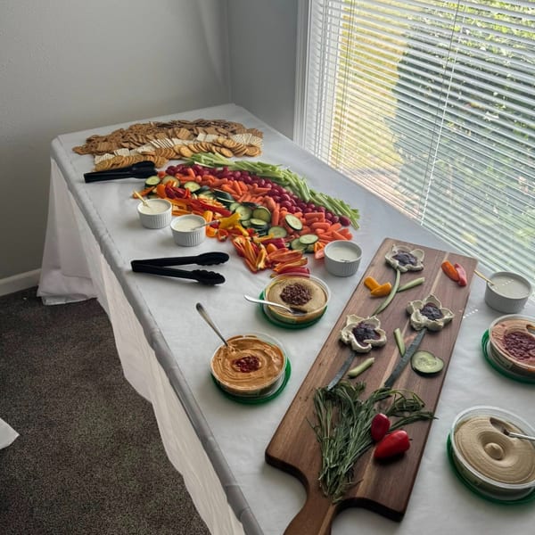 A long table covered with crackers, fresh vegetables, dips, and decorative hummus arrangements.