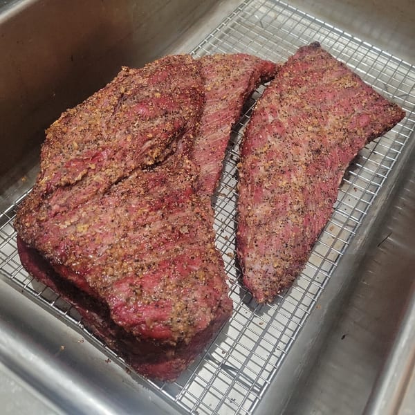 Two large cuts of raw, seasoned meat resting on a metal rack inside a stainless steel sink.