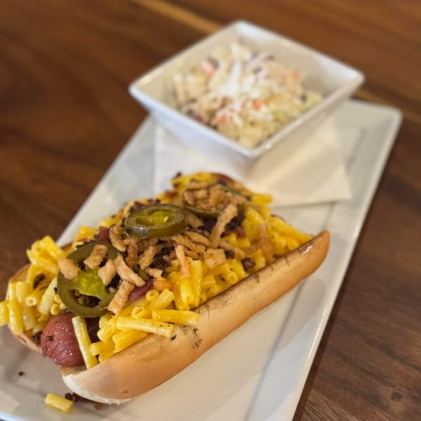A Rendezvous Bar & Grill hot dog topped with mac and cheese, jalapeños, and crispy onions, with coleslaw.