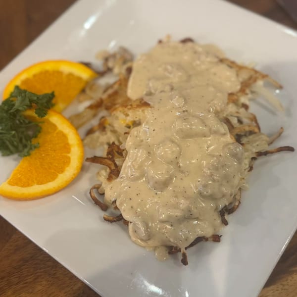 Hash browns topped with creamy gravy, garnished with orange slices and parsley on a white plate.
