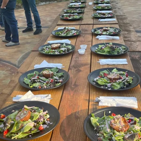Long wooden table set with multiple plates of fresh salads, ready for guests at Rendezvous Bar & Grill.