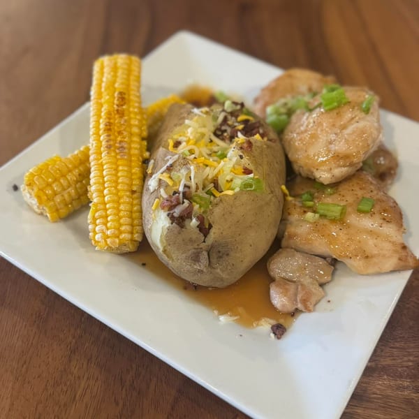 A Rendezvous Bar & Grill plate with grilled chicken, a loaded baked potato, and corn on the cob.
