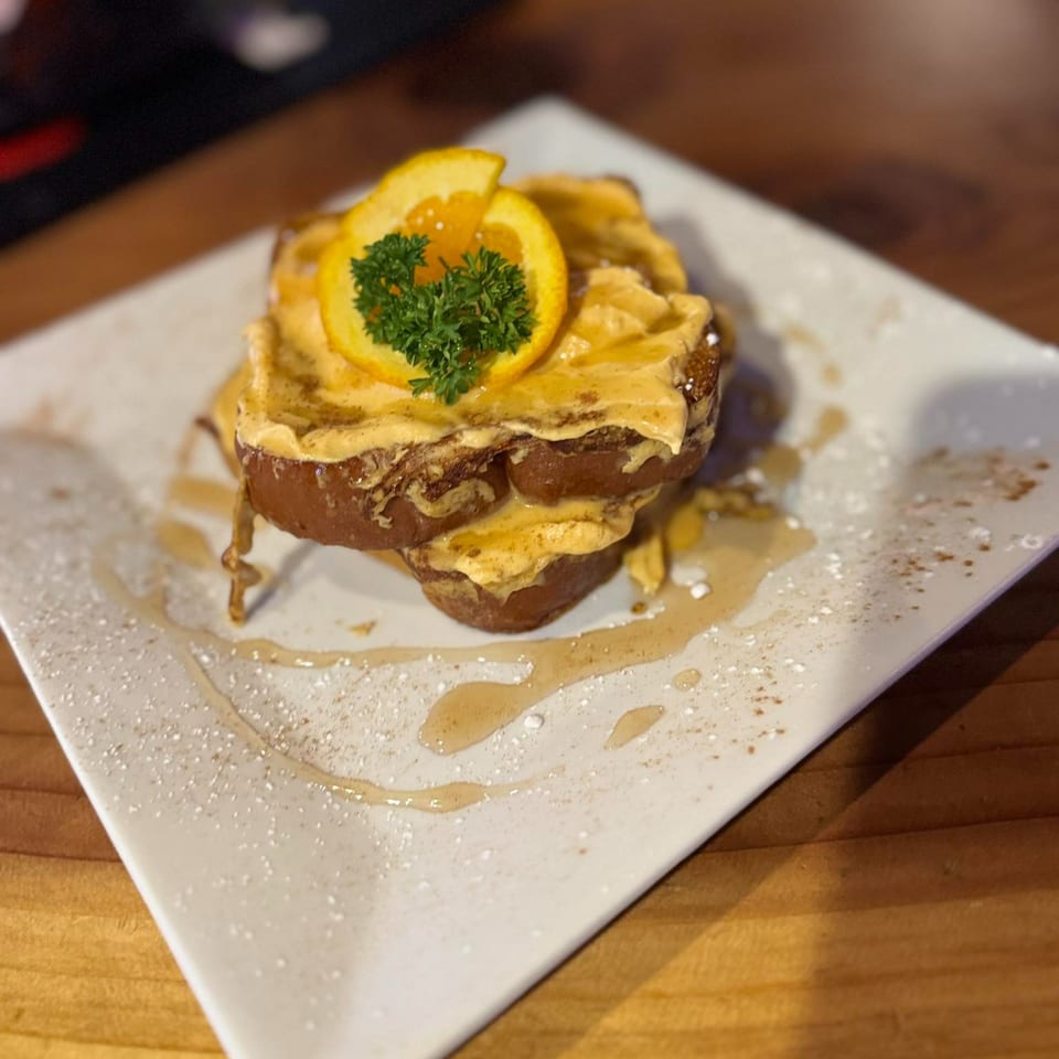 Two slices of French toast topped with orange cream, an orange slice, and parsley, drizzled with syrup.